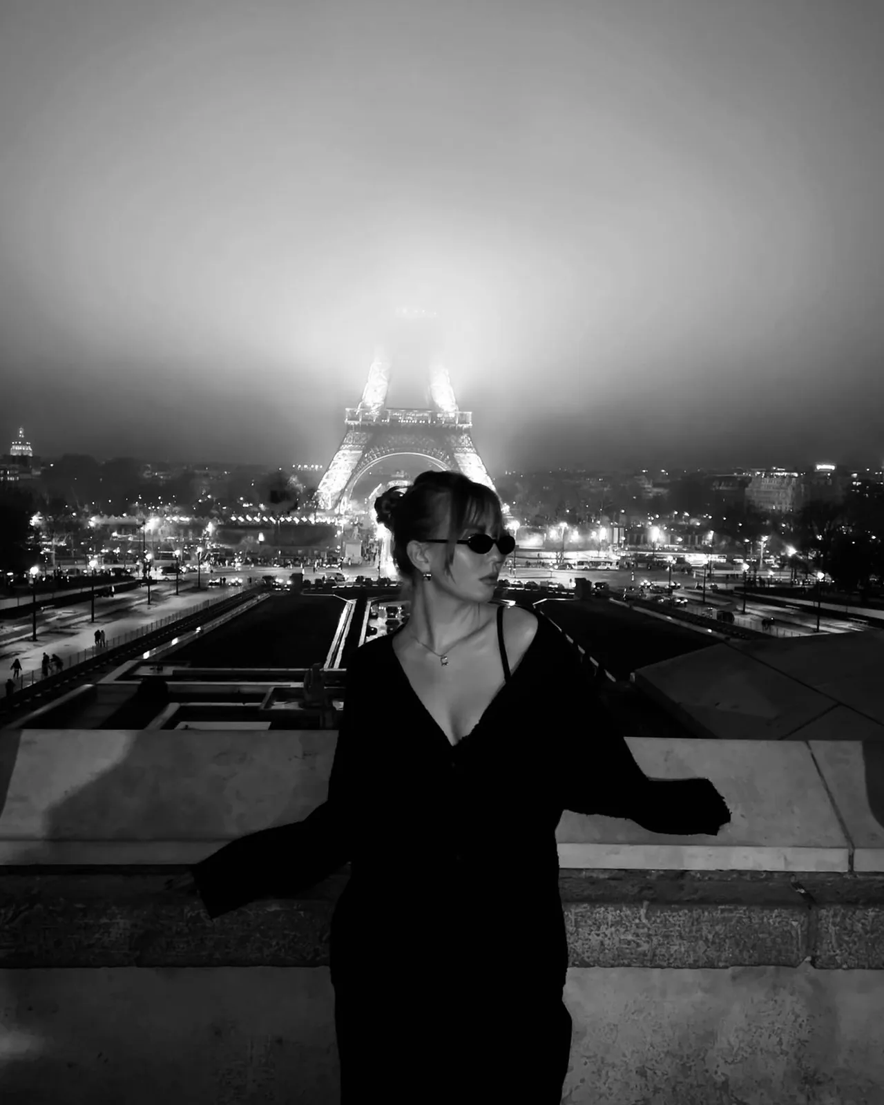 sofia in sunglasses in front of the Eiffel Tower in the fog, black and white